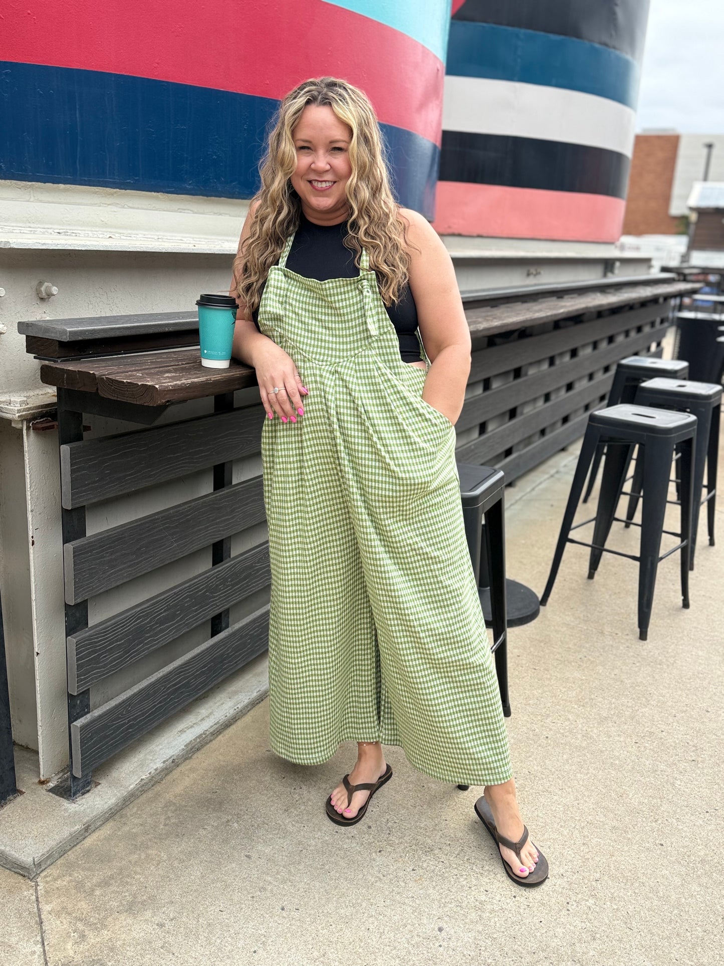 Woman in a green checkered dress standing outdoors with a colorful boat in the background.