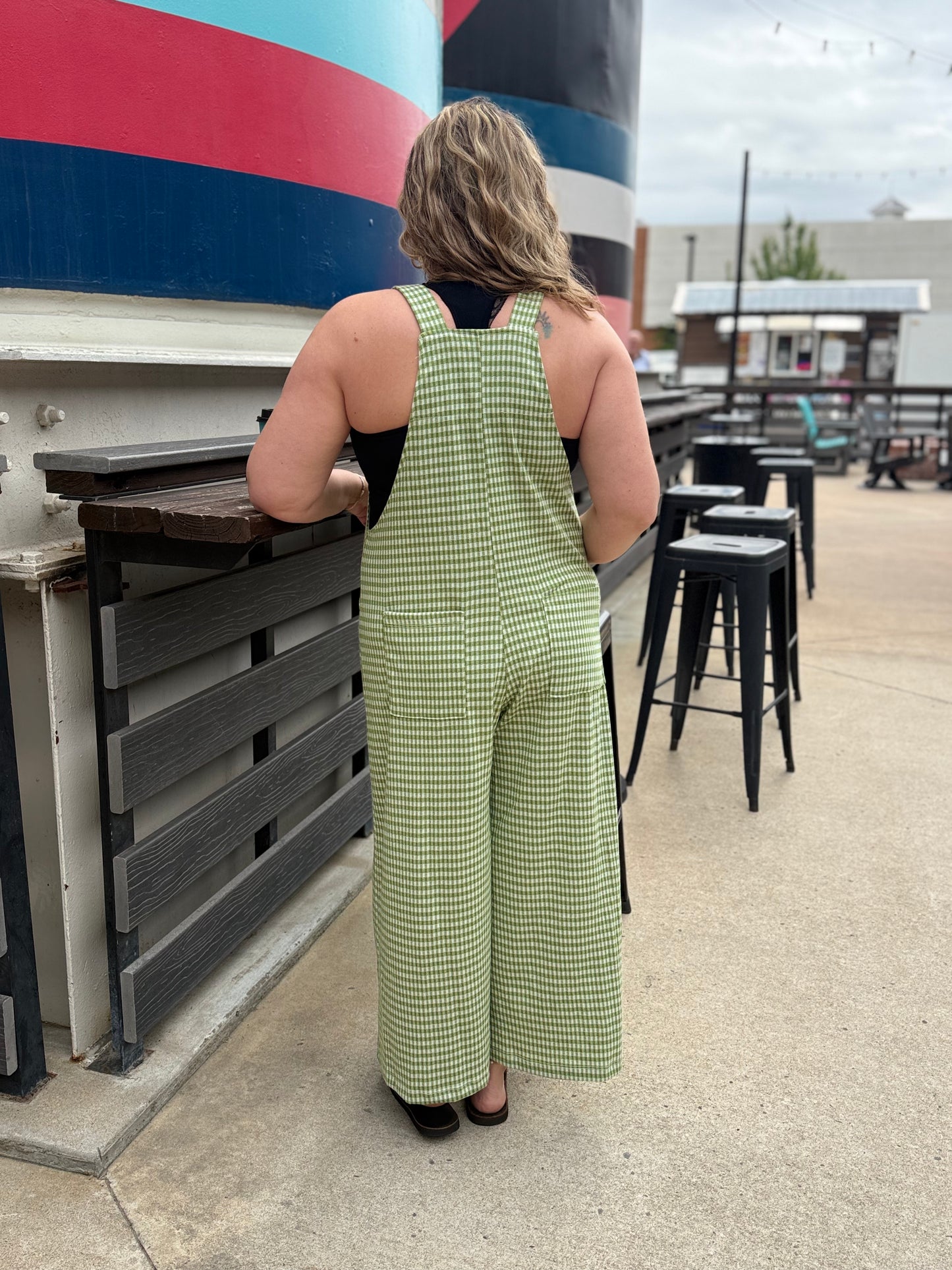 Person wearing a green checkered jumpsuit standing near a large cylindrical tank with a colorful stripe.