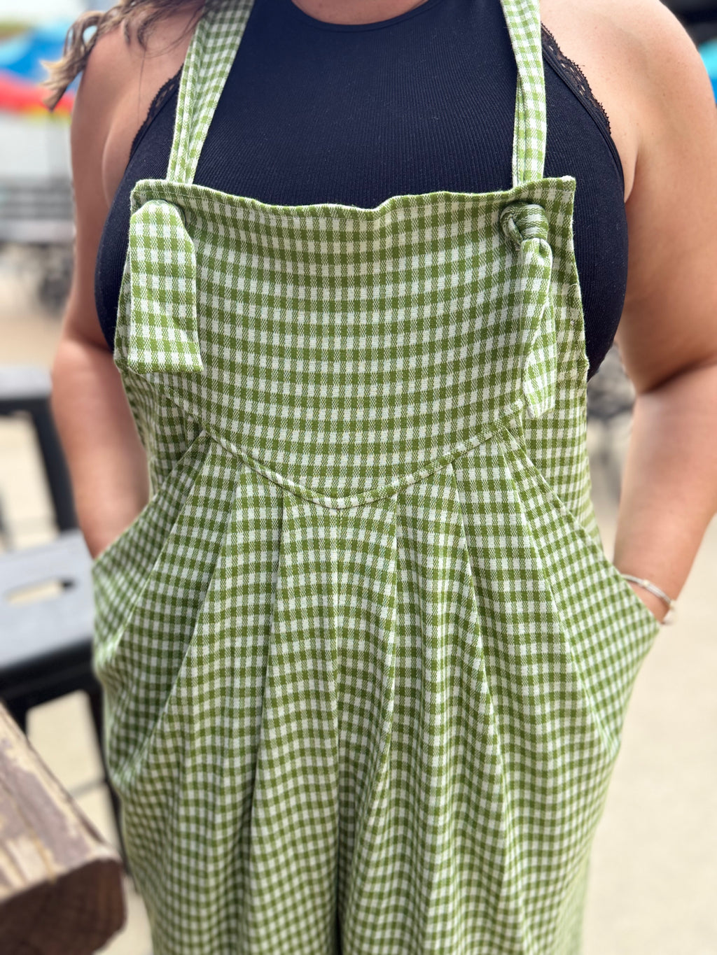 Person wearing a green checkered apron over a black top outdoors.