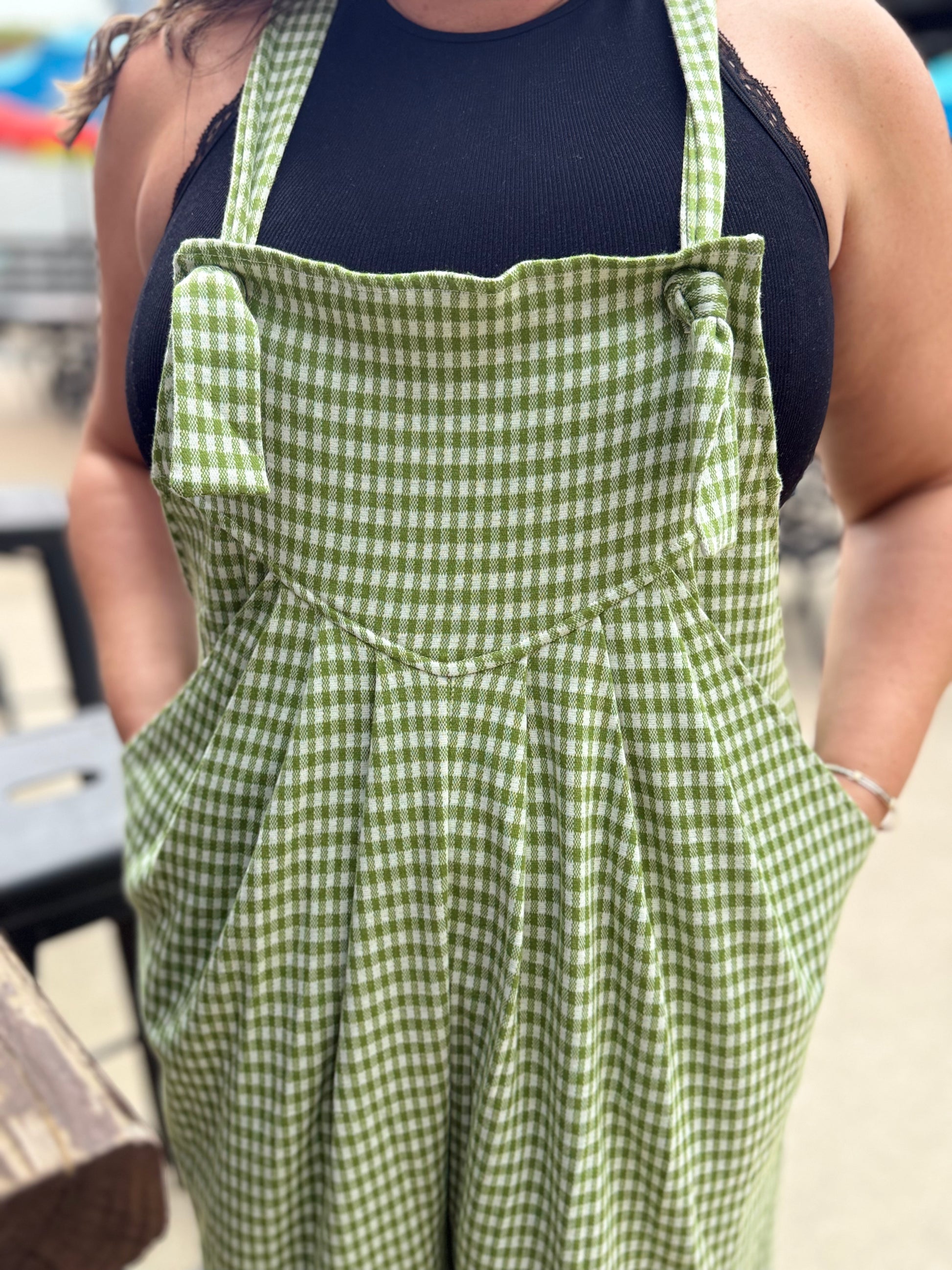Person wearing a green checkered apron over a black top outdoors.
