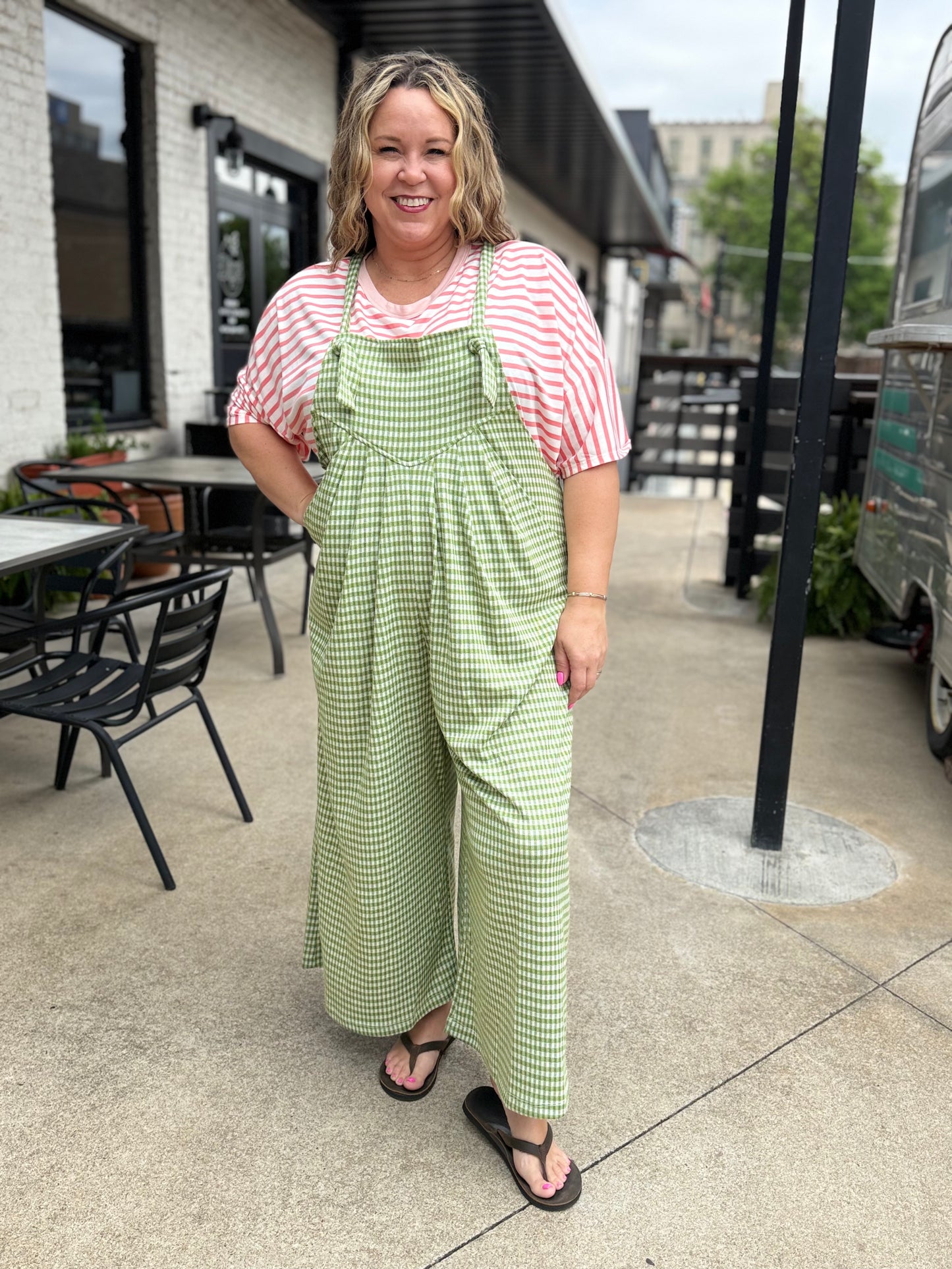 Woman wearing a red and white striped shirt with green checkered overalls standing on a sidewalk.