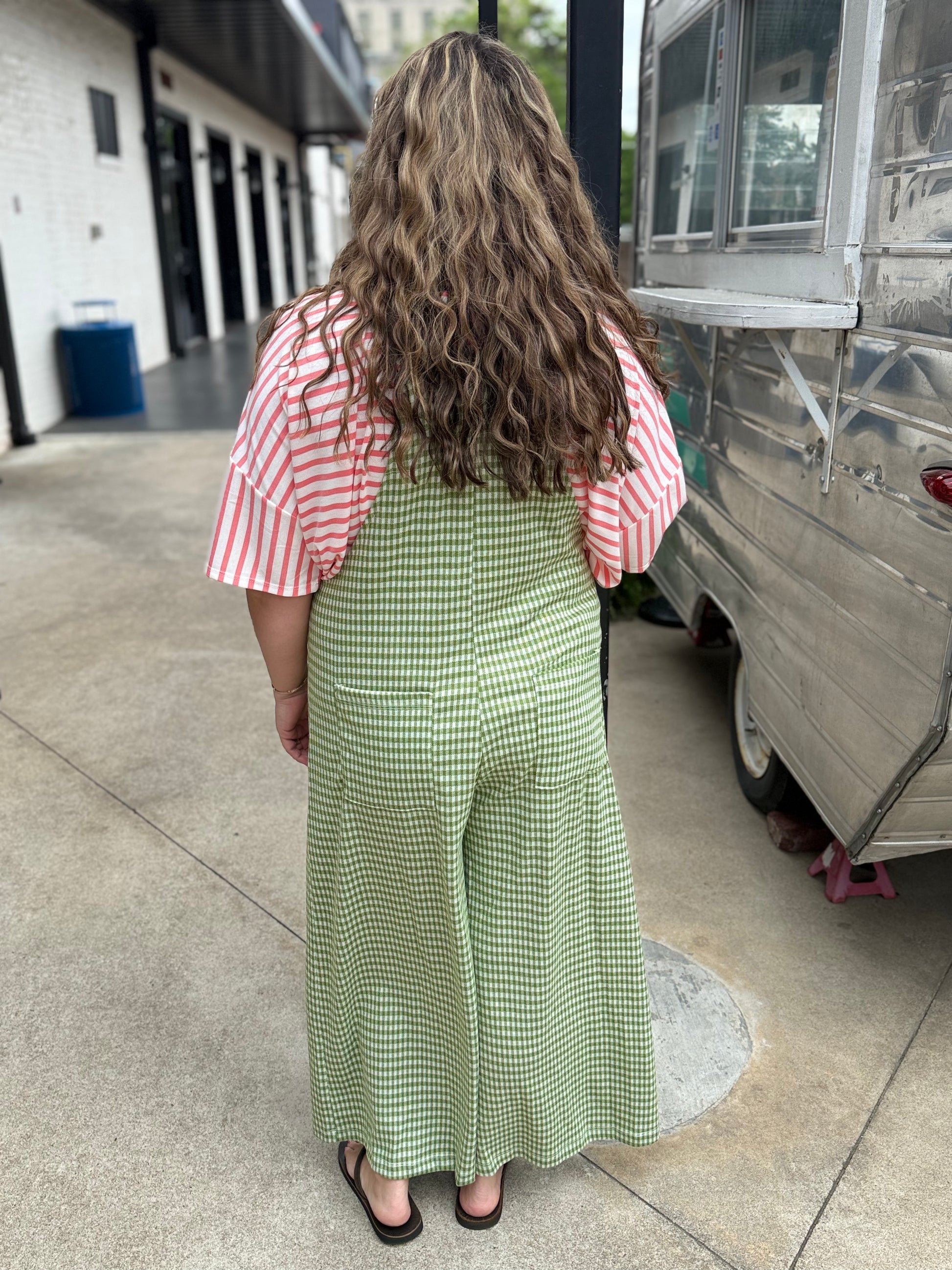 Woman in a green checkered dress and red striped shirt standing next to a food truck.