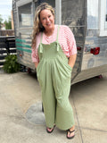 Woman wearing a red and white striped shirt and green checkered overalls standing in front of a vintage trailer.